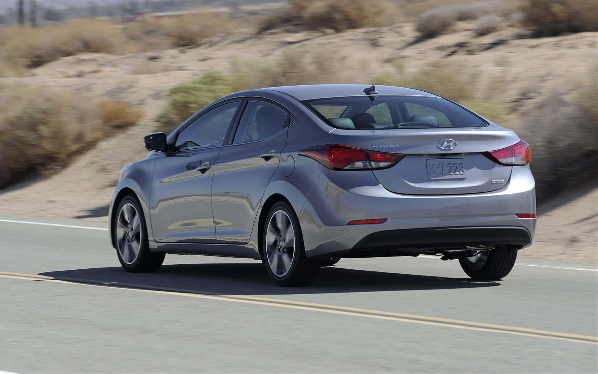 Hyundai Elantra 桌布 壁紙 — 一輛銀色現代Elantra在沙漠公路上行駛，背景是乾燥的灌木叢和山丘。