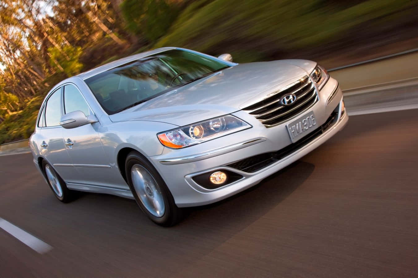 Hyundai Azera 桌布 壁紙 — 一輛銀色現代轎車在陽光明媚的道路上行駛，背景是模糊的樹木。