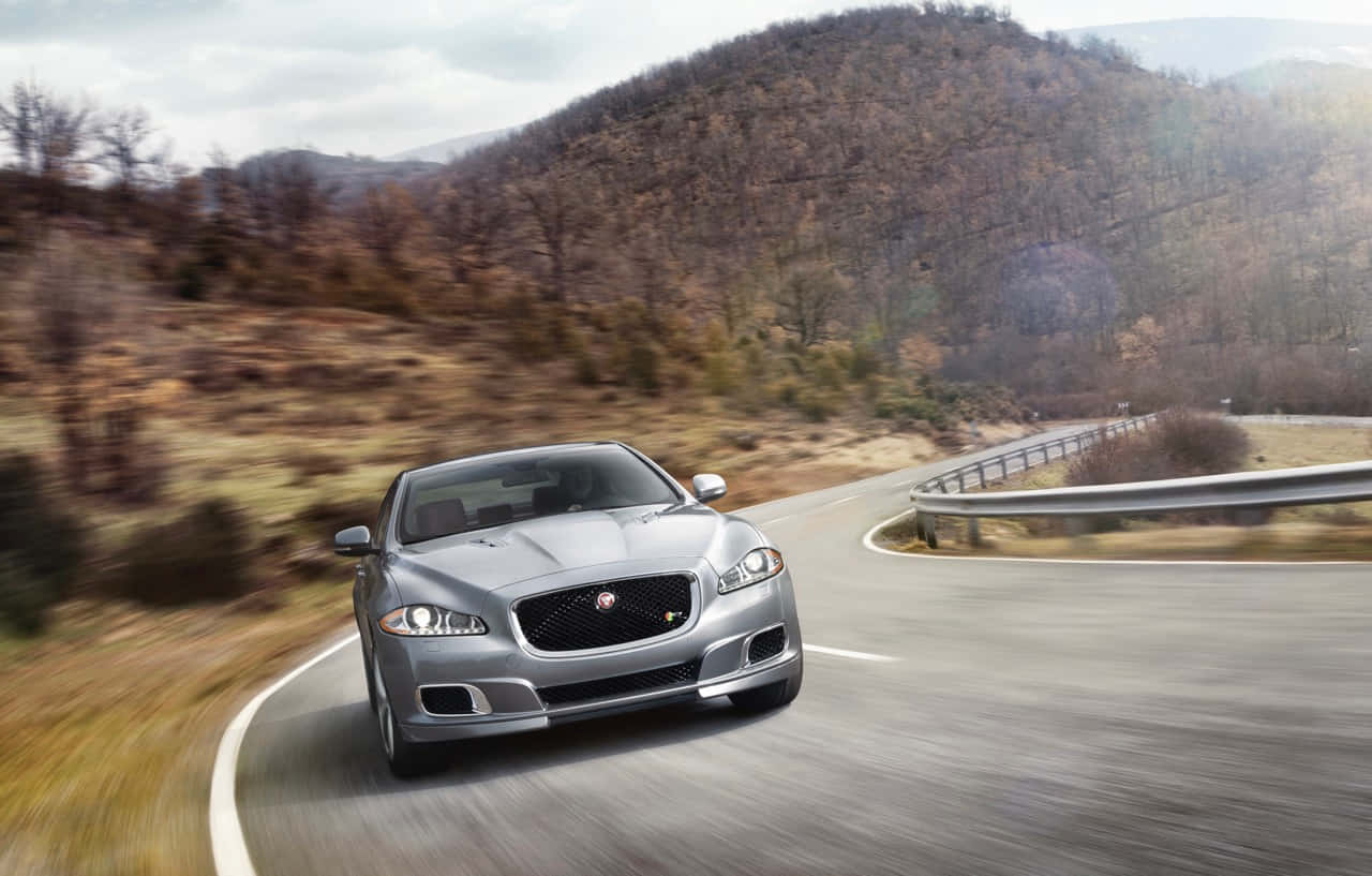 Jaguar Xjr 桌布 壁紙 — 一輛銀色積架跑車沿著蜿蜒的山路穿過秋葉飛馳。
