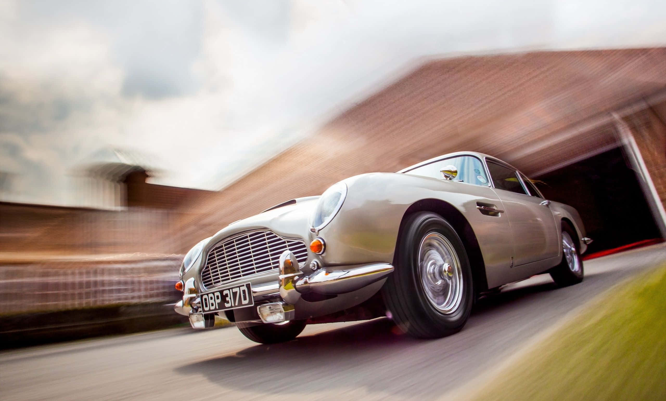 Aston Martin Db5 桌布 壁紙 — 一輛銀色經典Aston Martin在隧道中疾馳，道路和磚牆上帶有動態模糊效果。
