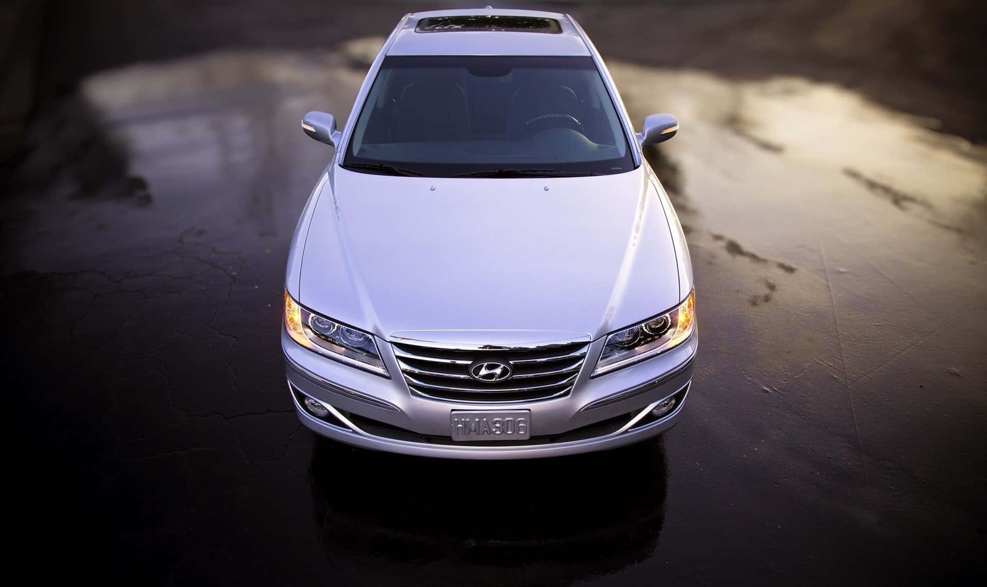 Hyundai Azera 桌布 壁紙 — 一輛銀色豪華轎車在金色夕陽下閃閃發光，停在濕漉漉的瀝青路中央。
