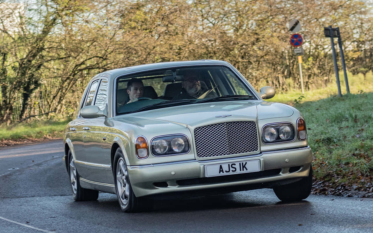 Bentley Arnage 桌布 壁紙 — 一輛銀色賓利雅致沿著綠樹成蔭的鄉村道路行駛，車內有兩名男子。