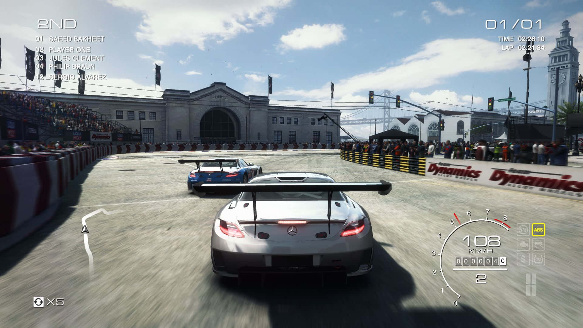 Grid Autosport 桌布 壁紙 — 一輛銀色賽車在陽光明媚的賽道上疾馳，前方有一輛藍色對手，觀眾在明亮的藍天下歡呼。