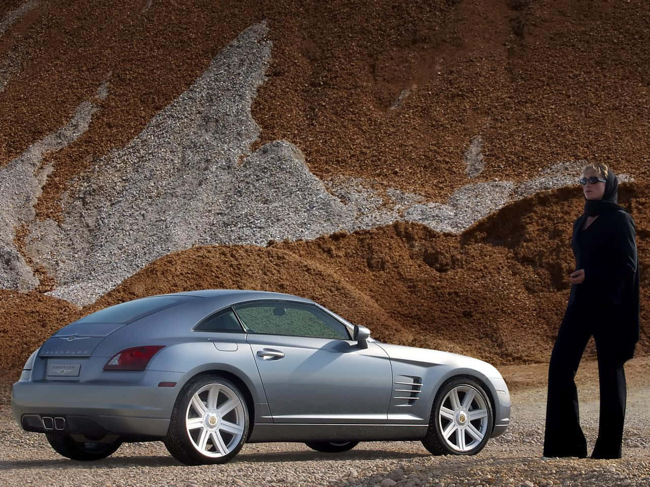 Chrysler Crossfire 桌布 壁紙 — 一輛銀色跑車在一位身穿黑衣的女子旁邊閃閃發光，背景是崎嶇的泥土和礫石。
