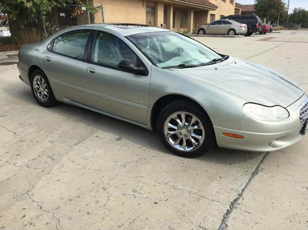 Chrysler Lhs 桌布 壁紙 — 一輛銀色轎車停泊在裂開的混凝土車道上，背景是米色房屋和其他車輛。