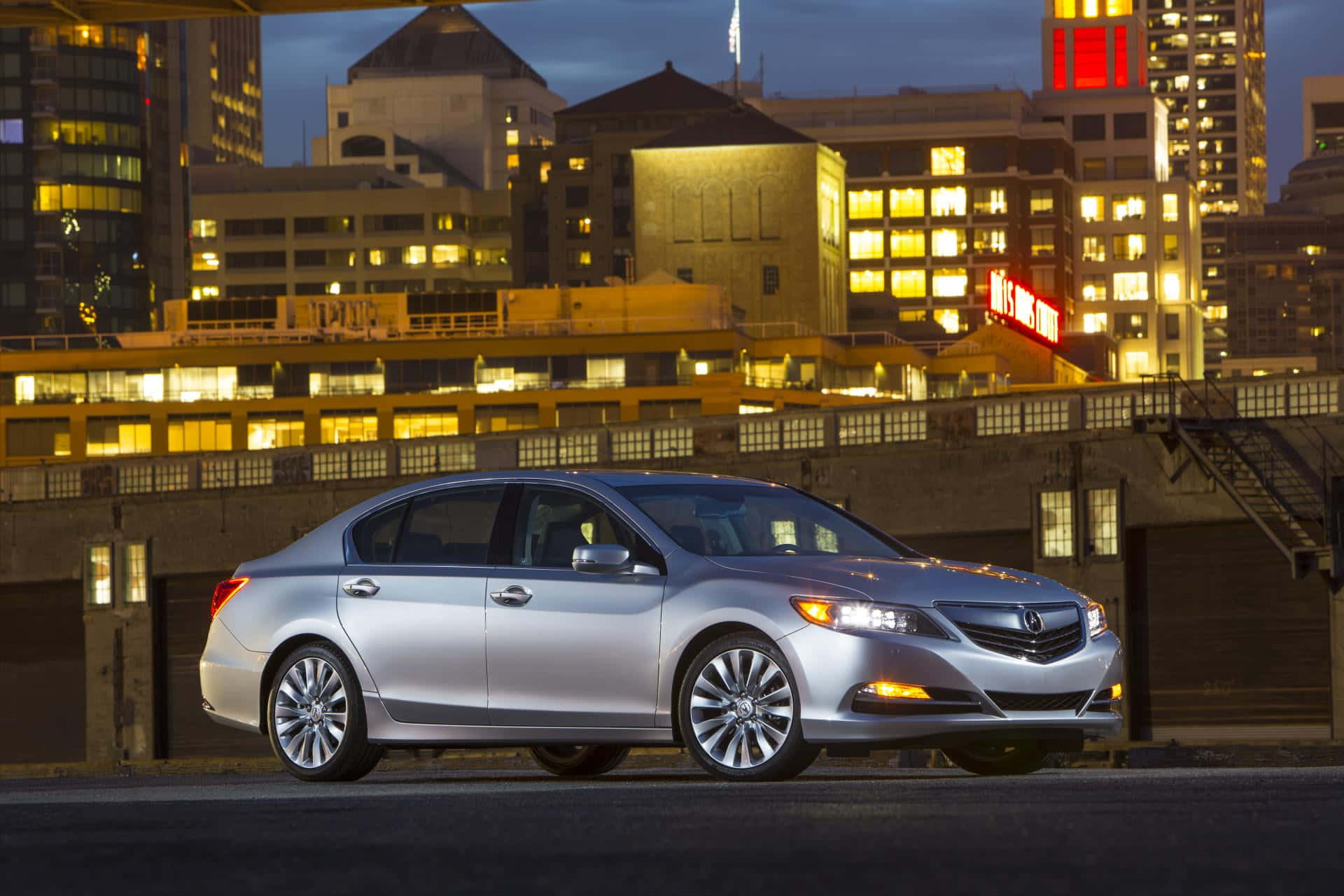 Acura Rlx 桌布 壁紙 — 一輛銀色轎車在暮色城市燈光下閃耀，背景是燈火通明的摩天大樓。