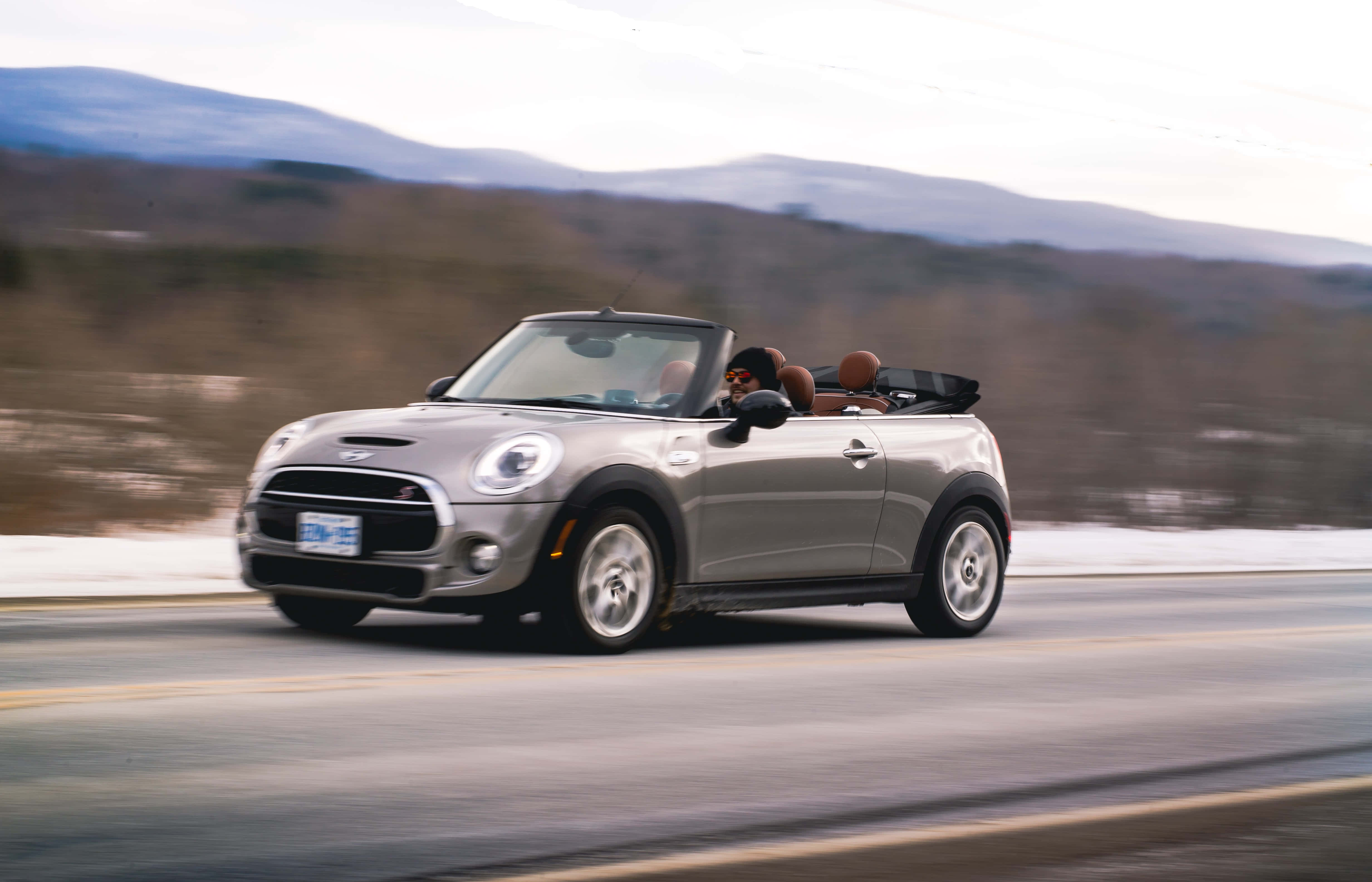 Mini Cooper S Convertible 桌布 壁紙 — 一輛銀色開篷跑車在雪路上飛馳，背景是模糊的山巒。