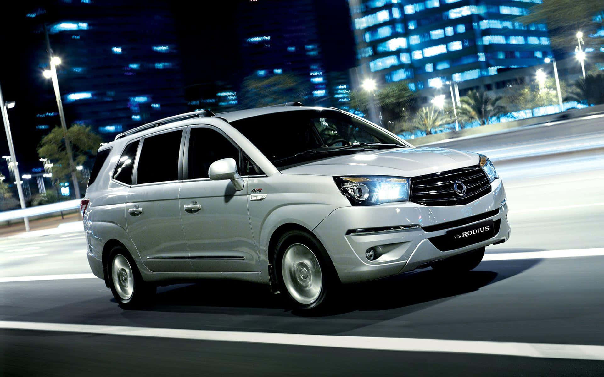 Ssangyong 桌布 壁紙 — 一輛銀色雙龍Rodius小型貨車在霓虹燈閃爍的城市夜間高速行駛，留下模糊的動態軌跡。