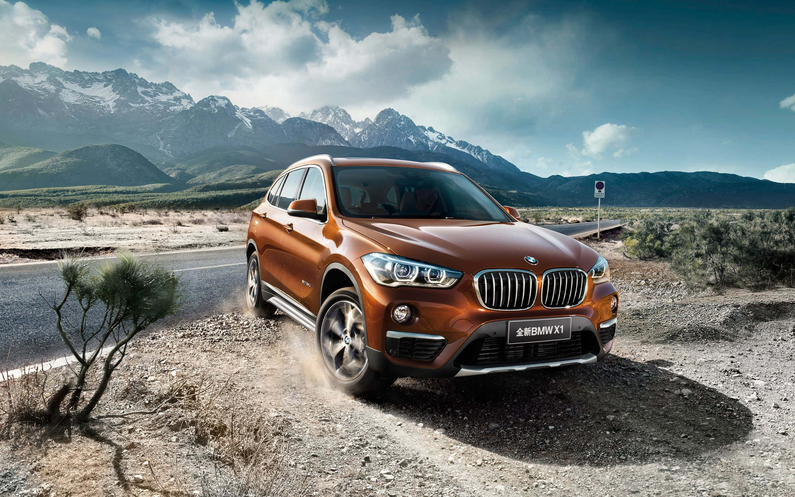 Bmw I8 桌布 壁紙 — 一輛銅色BMW X1 SUV在部分多雲的天空下，行駛在沙漠公路上，背景是雪山。