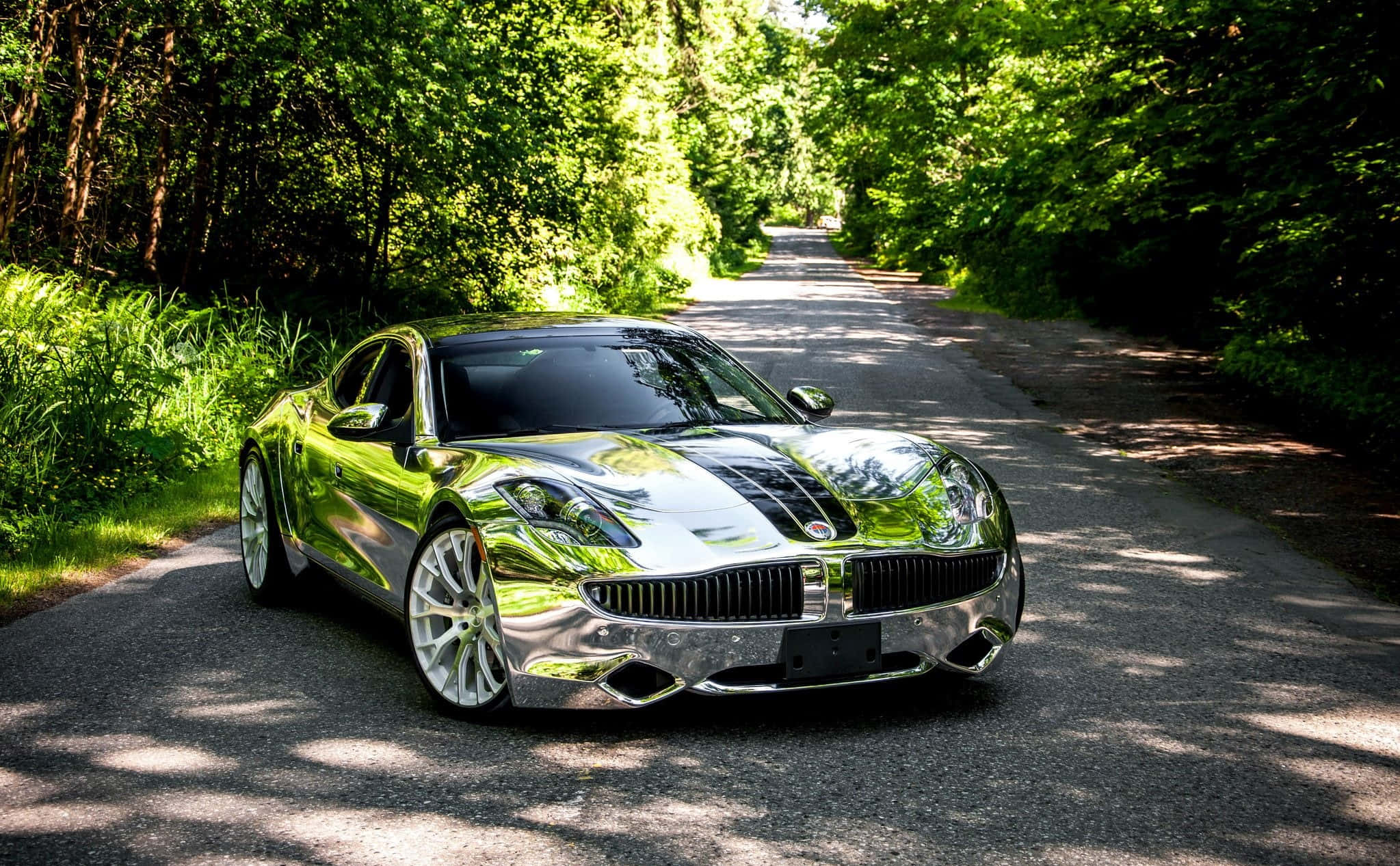 Fisker 桌布 壁紙 — 一輛鍍鉻跑車在樹木成蔭的森林道路上，斑駁的陽光下閃閃發光。
