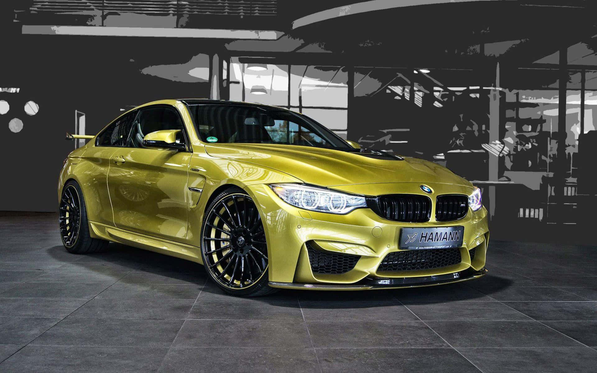 型格自訂調校跑車動感馳騁 壁紙 — 一輛閃亮的金色Hamann改裝BMW M4雙門跑車，在時尚的工業車庫中展示，背景為單色。