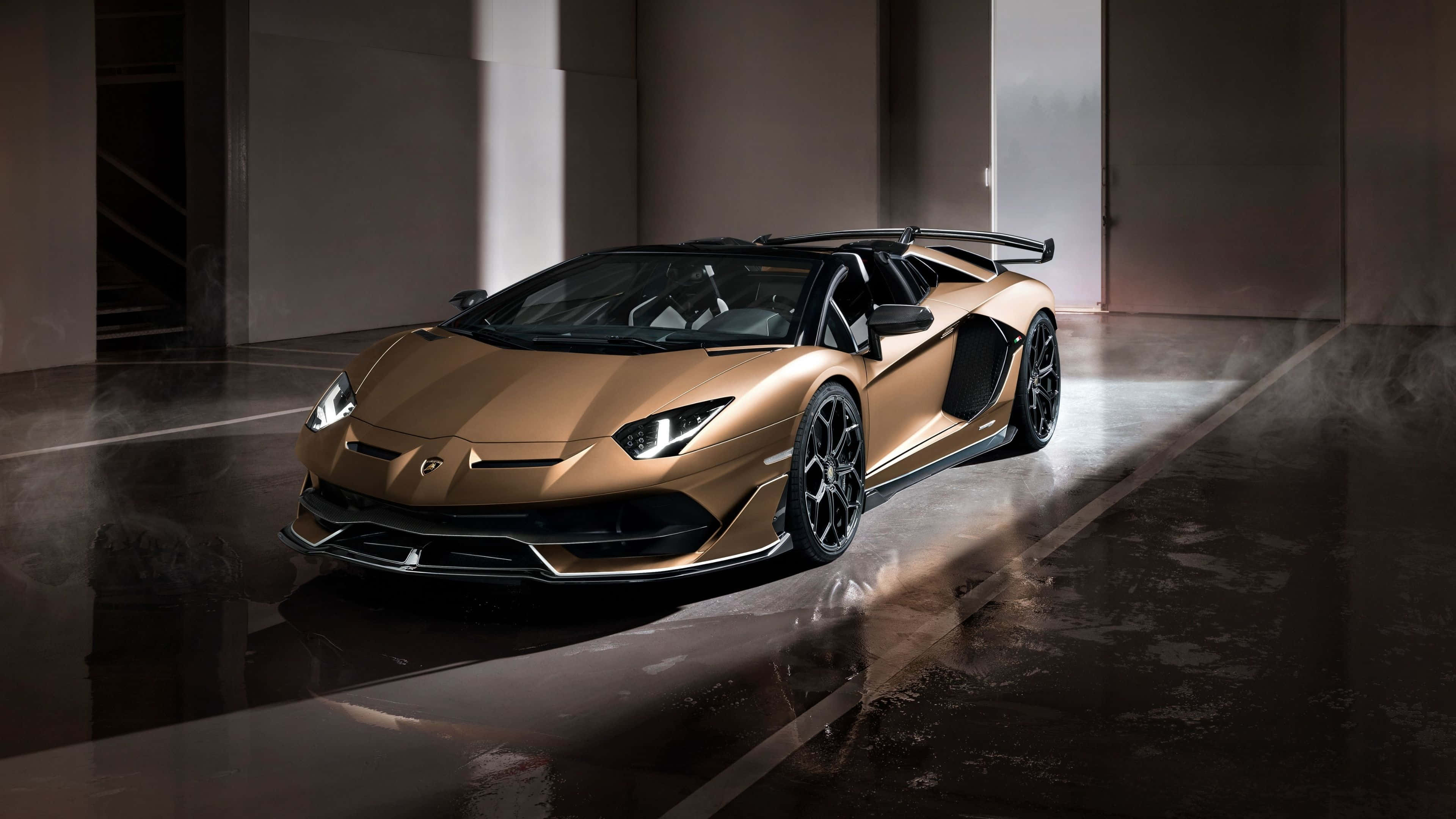 林寶堅尼 4K 桌布 壁紙 — 一輛閃亮的金色林寶堅尼 Aventador SVJ Roadster 停放在燈光昏暗的工業車庫中，帶有戲劇性的聚光燈效果。