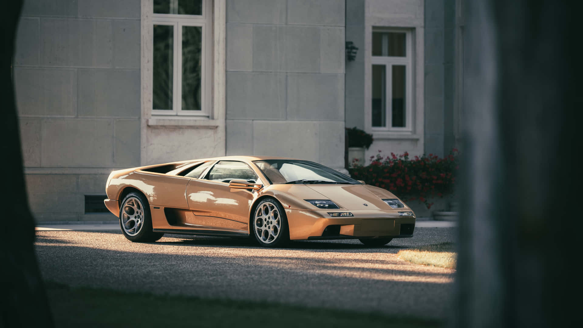 Lamborghini Diablo 桌布 壁紙 — 一輛閃閃發光的金色林寶堅尼 Diablo 停泊在石砌大宅前，陽光投下長長的影子。