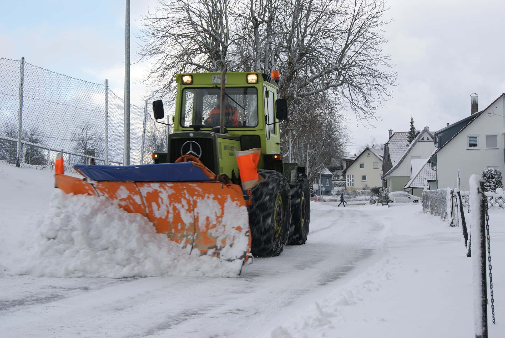 Snowplow 桌布 壁紙 — 一輛青檸綠色的掃雪車在多雲的冬日天空下清理積雪的住宅街道。