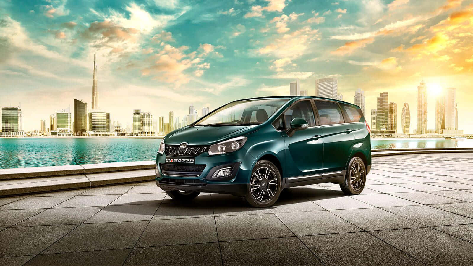 Mahindra 桌布 壁紙 — 一輛青綠色的Marazzo小型貨車停泊在瓷磚鋪設的海濱長廊上，背景是杜拜天際線和哈利法塔，沐浴在金色的日落光芒中。