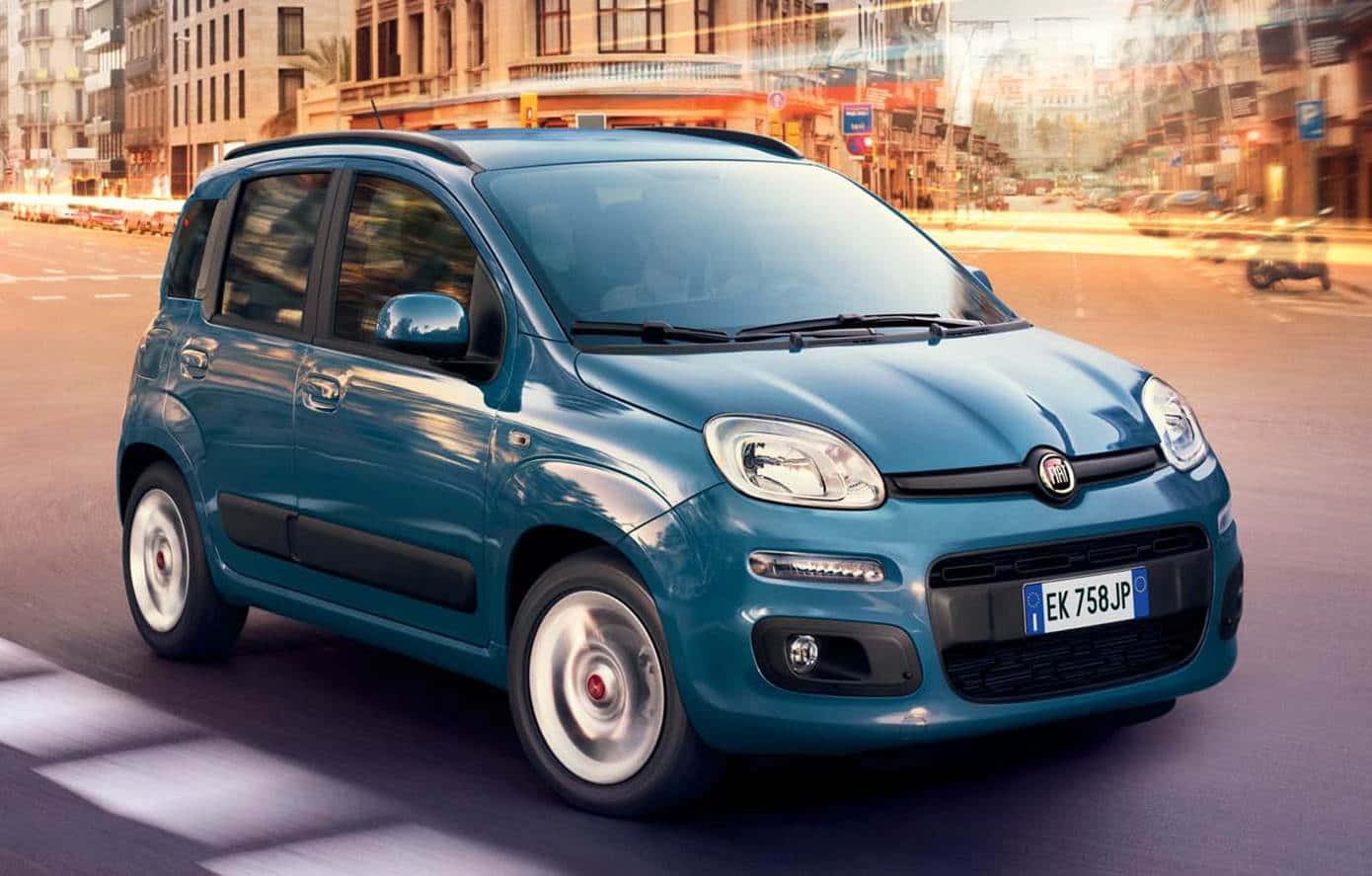Fiat Panda 桌布 壁紙 — 一輛青綠色的菲亞特熊貓車在陽光明媚的城市街道上行駛，帶有模糊的動態和溫暖的黃金時段光線。