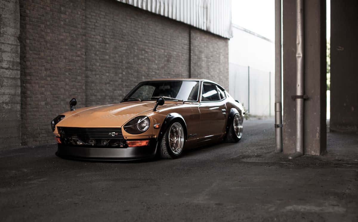 Datsun 桌布 壁紙 — 一輛青銅色經典跑車配備定制輪圈，在漫射光下低伏於粗糙的工業倉庫中。