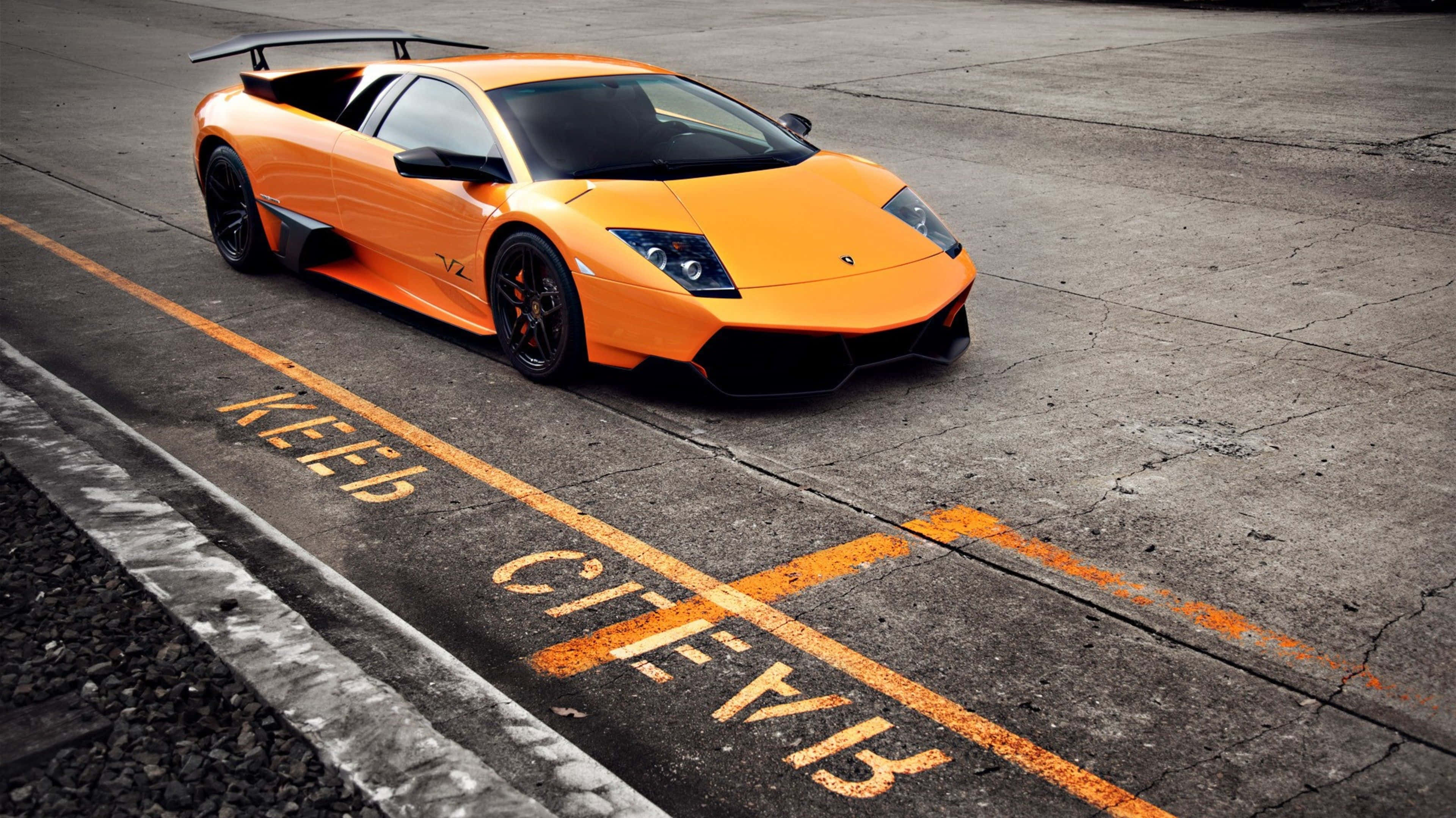 Lamborghini Murciélago 桌布 壁紙 — 一輛鮮橙色的林寶堅尼 Murciélago 停放在一條有裂痕的瀝青賽道上，賽道上有褪色的 'KEEP CLEAR' 標記。