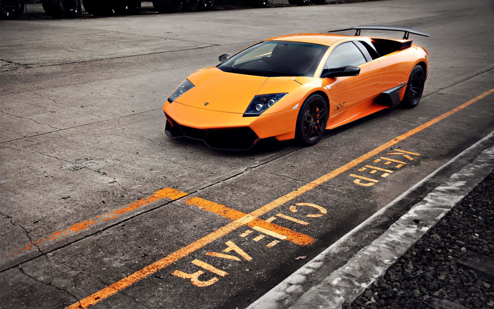 Lamborghini Murciélago 桌布 壁紙 — 一輛鮮橙色的林寶堅尼 Murciélago 停放在一個佈滿裂縫、帶有褪色 'KEEP CLEAR' 標記的混凝土場地上。