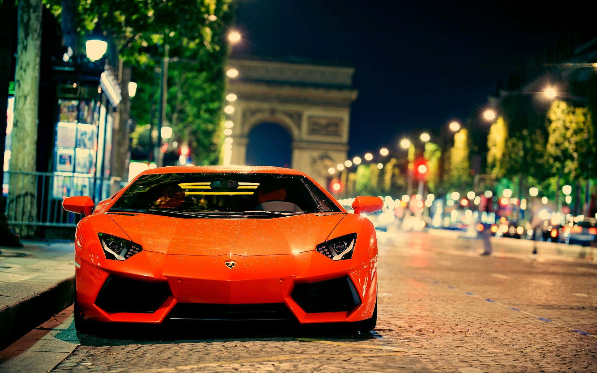 HD Car 桌布 壁紙 — 一輛鮮橙色的林寶堅尼Aventador停泊在夜晚的鵝卵石街道上，背景中凱旋門閃耀著光芒。