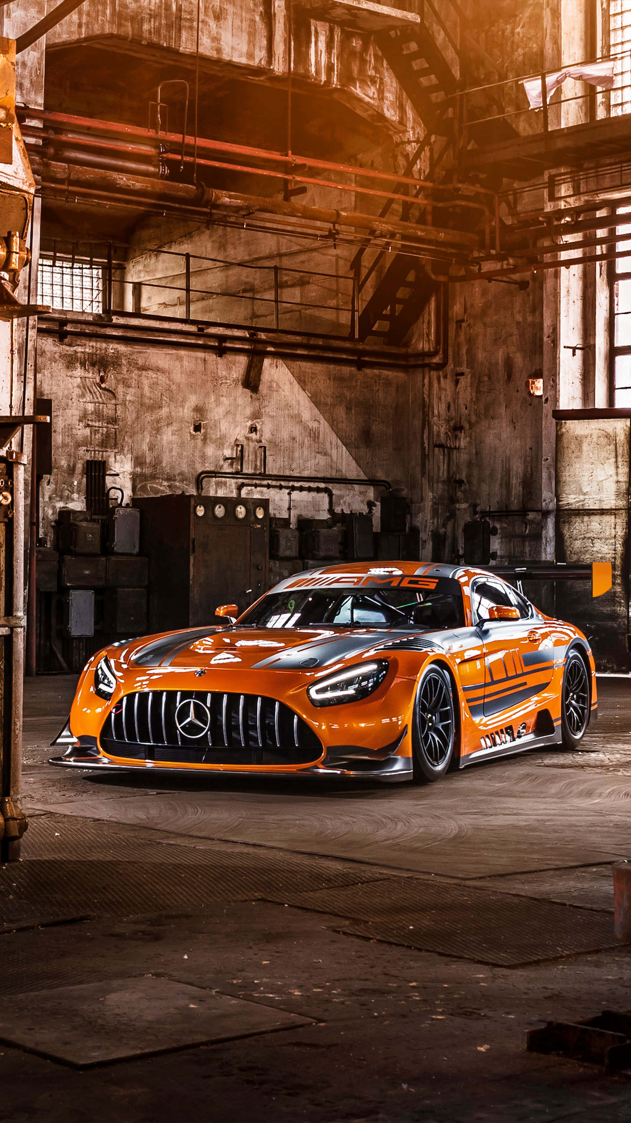 4K Mercedes 桌布 壁紙 — 一輛鮮橙色的梅賽德斯-AMG GT3賽車在風化倉庫內的溫暖工業照明下閃閃發光。