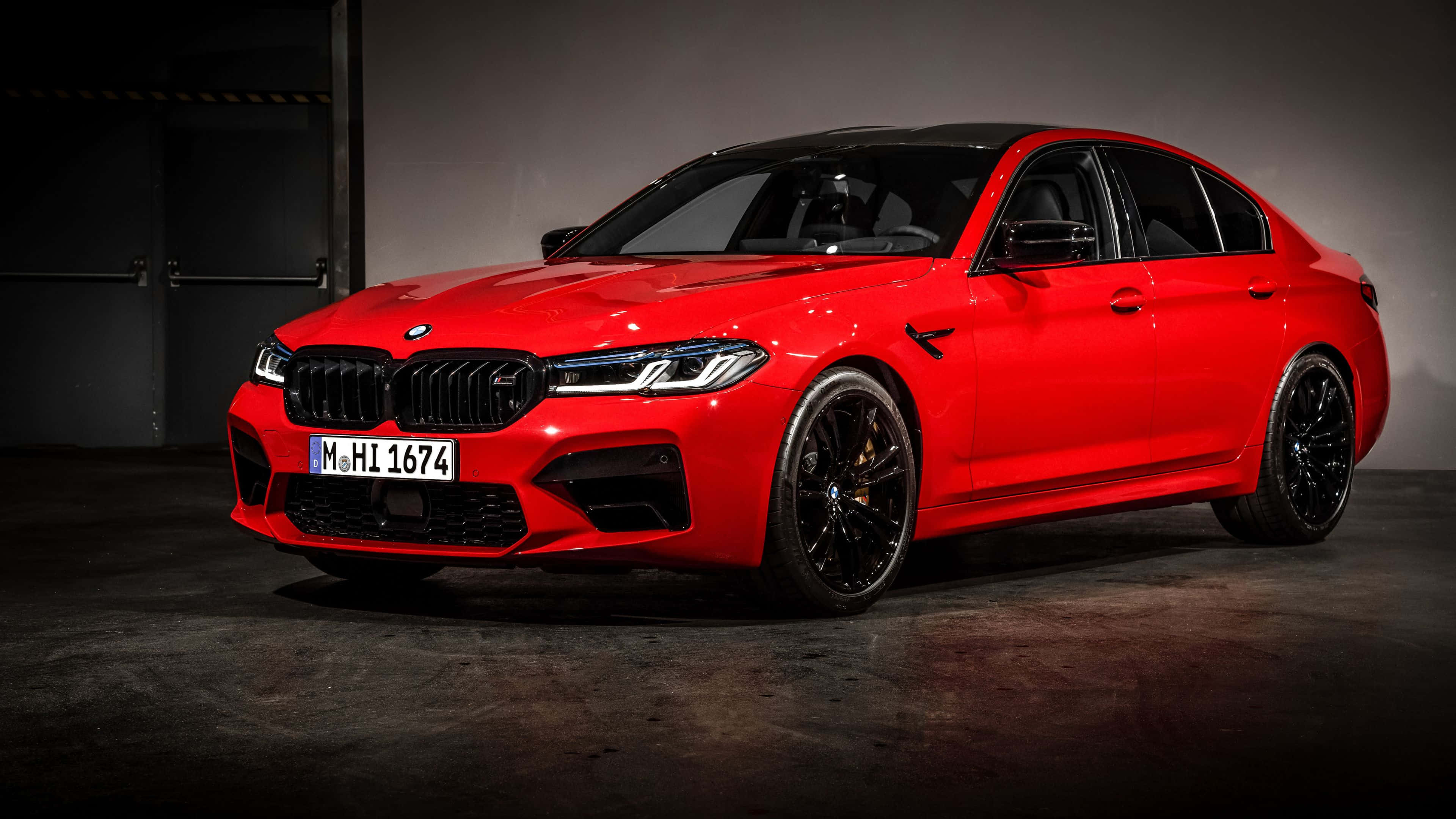 4K BMW 壁紙 桌布 壁紙 — 一輛鮮紅色BMW M5房車，帶有黑色飾件和光澤表面，在光線昏暗的工業車庫中展示。
