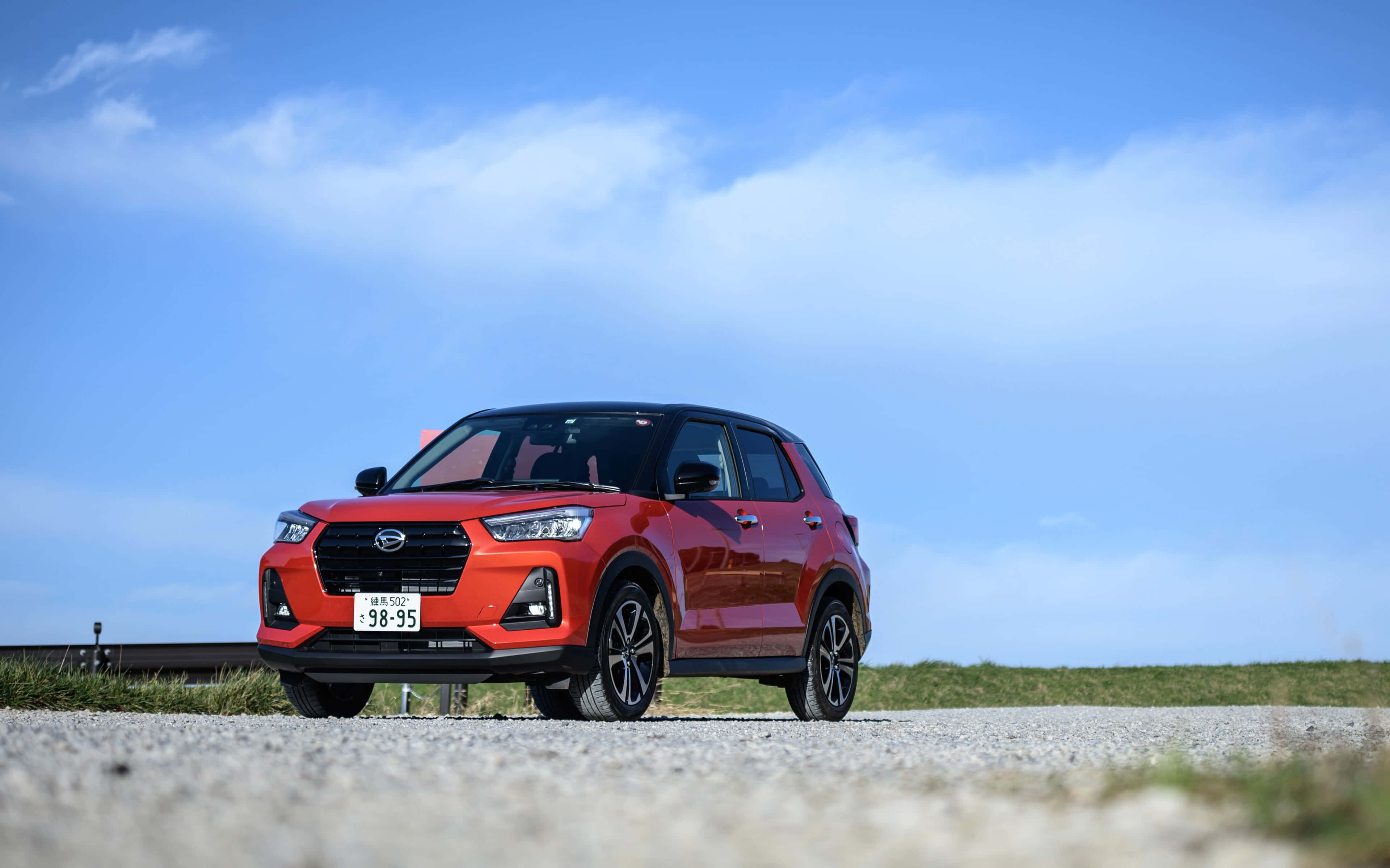 Daihatsu 桌布 壁紙 — 一輛鮮紅色SUV停泊在碎石路上，天空湛藍，白雲點綴。