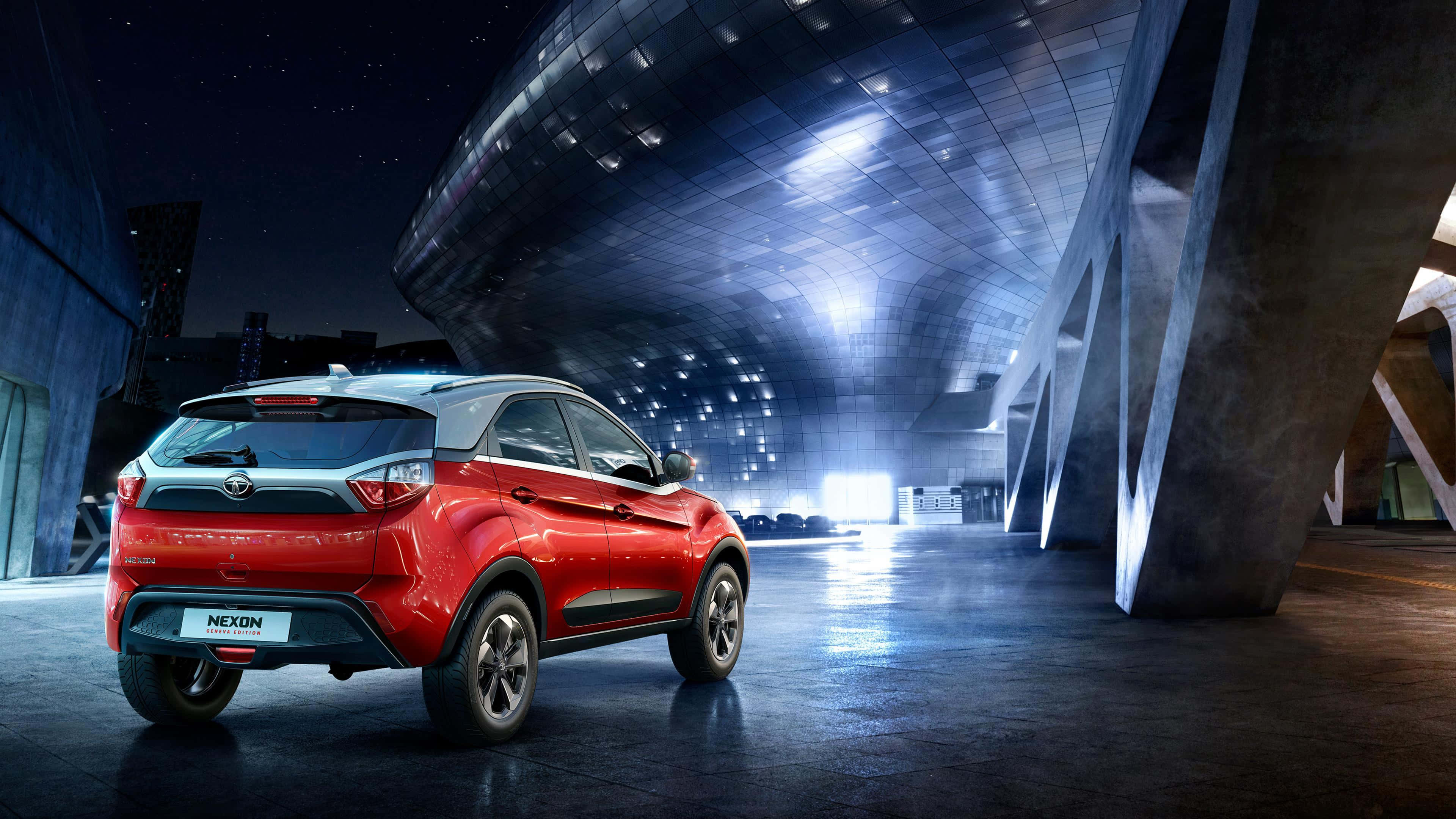 Tata Motors 桌布 壁紙 — 一輛鮮紅色SUV在夜晚停泊在未來主義曲線建築下，發光的燈光在濕漉漉的路面上反射。