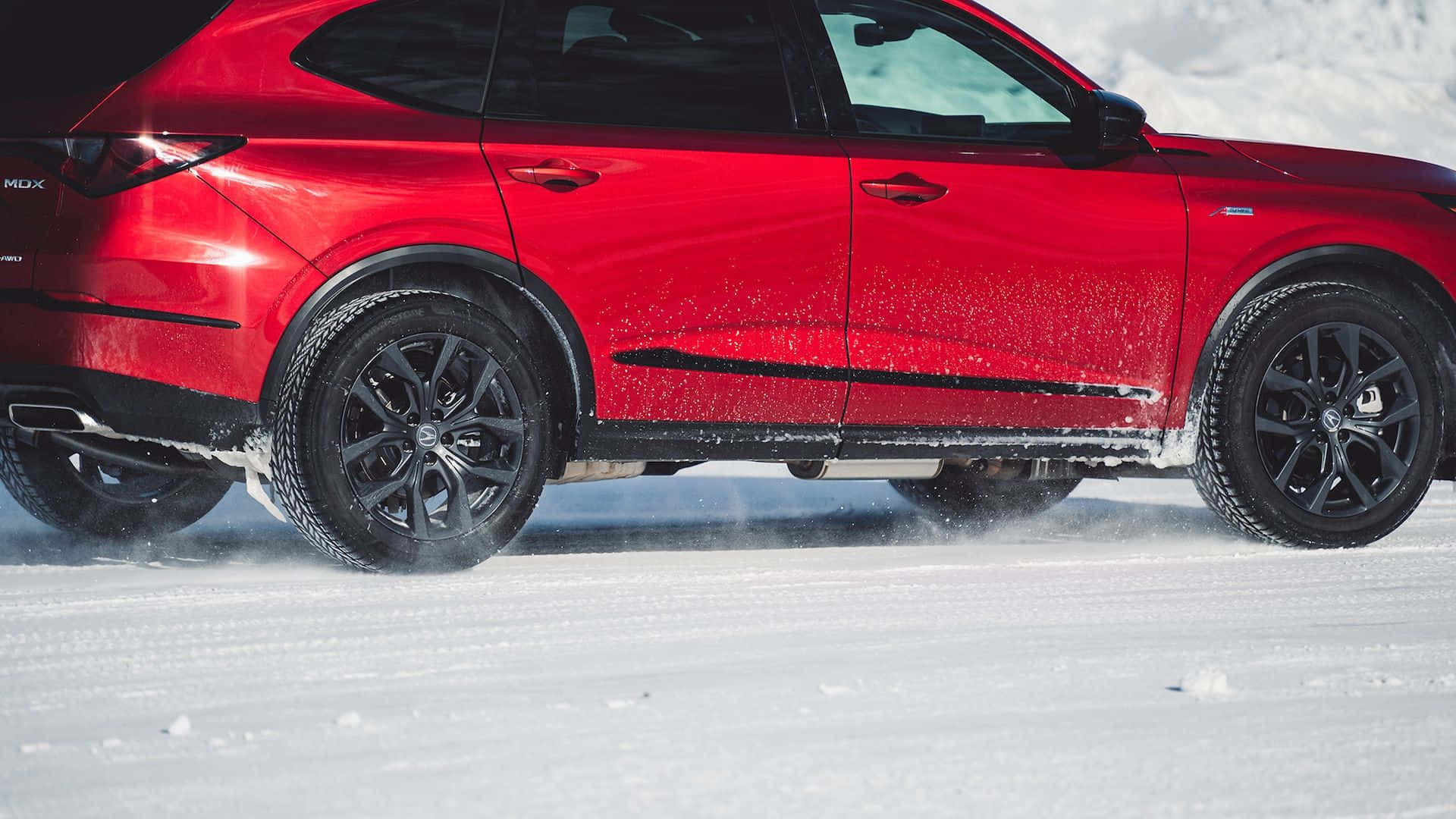 Winter Tires 桌布 壁紙 — 一輛鮮紅色SUV在明亮的日光下，以黑色車輪揚起粉雪，強勁地駛過新雪。
