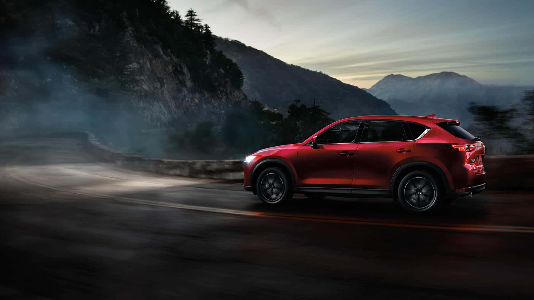 Mazda Cx-5 桌布 壁紙 — 一輛鮮紅色SUV在黃昏時分沿著蜿蜒的山路疾馳，霧氣在彎道周圍盤旋。