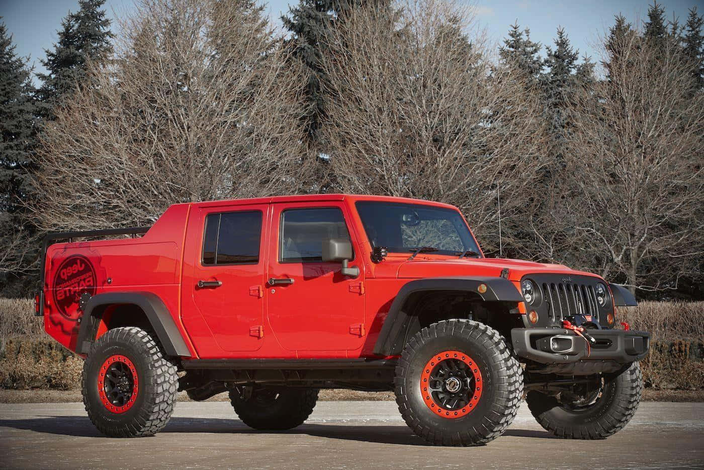 Jeep Gladiator 桌布 壁紙 — 一輛鮮紅色升高嘅Jeep Wrangler，配備超大輪胎，大膽咁企喺鋪砌嘅路面上，周圍係光禿禿嘅冬天樹木。