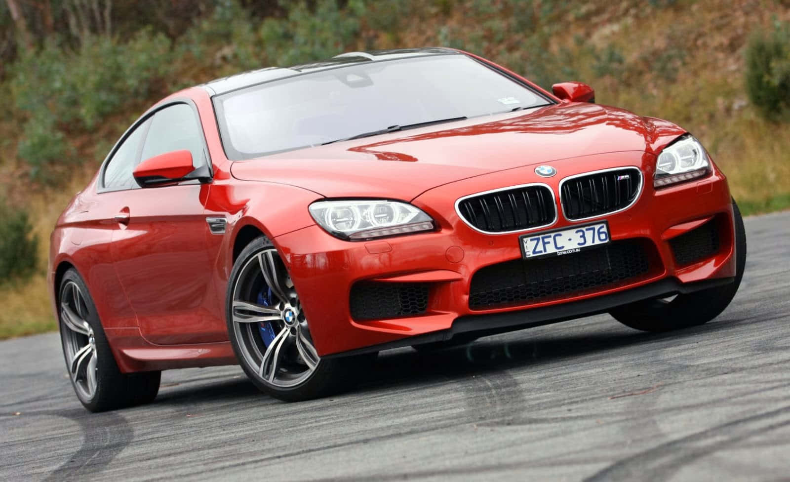 Bmw M6 桌布 壁紙 — 一輛鮮紅色嘅BMW M6轎跑車喺蜿蜒嘅道路上閃耀，背景係模糊嘅綠色植物。