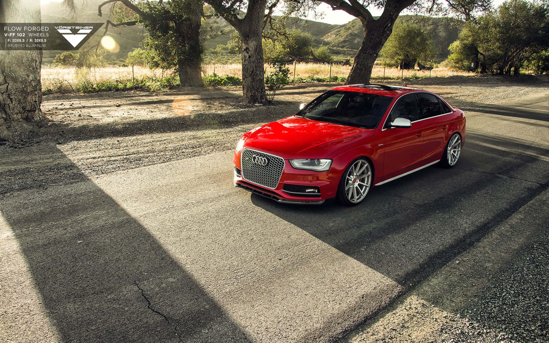 Audi S4 桌布 壁紙 — 一輛鮮紅色嘅奧迪跑車停泊喺陽光普照嘅碎石路上，大樹底下，背景係連綿起伏嘅山丘。