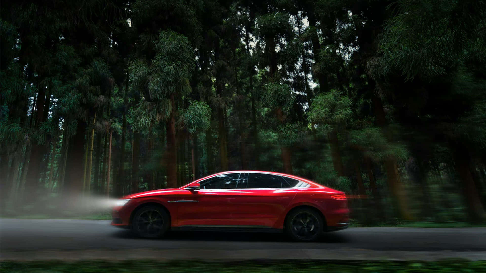 tesla 桌布 壁紙 — 一輛鮮紅色房車在茂密森林中高速行駛，車輪帶出動態模糊和霧氣。