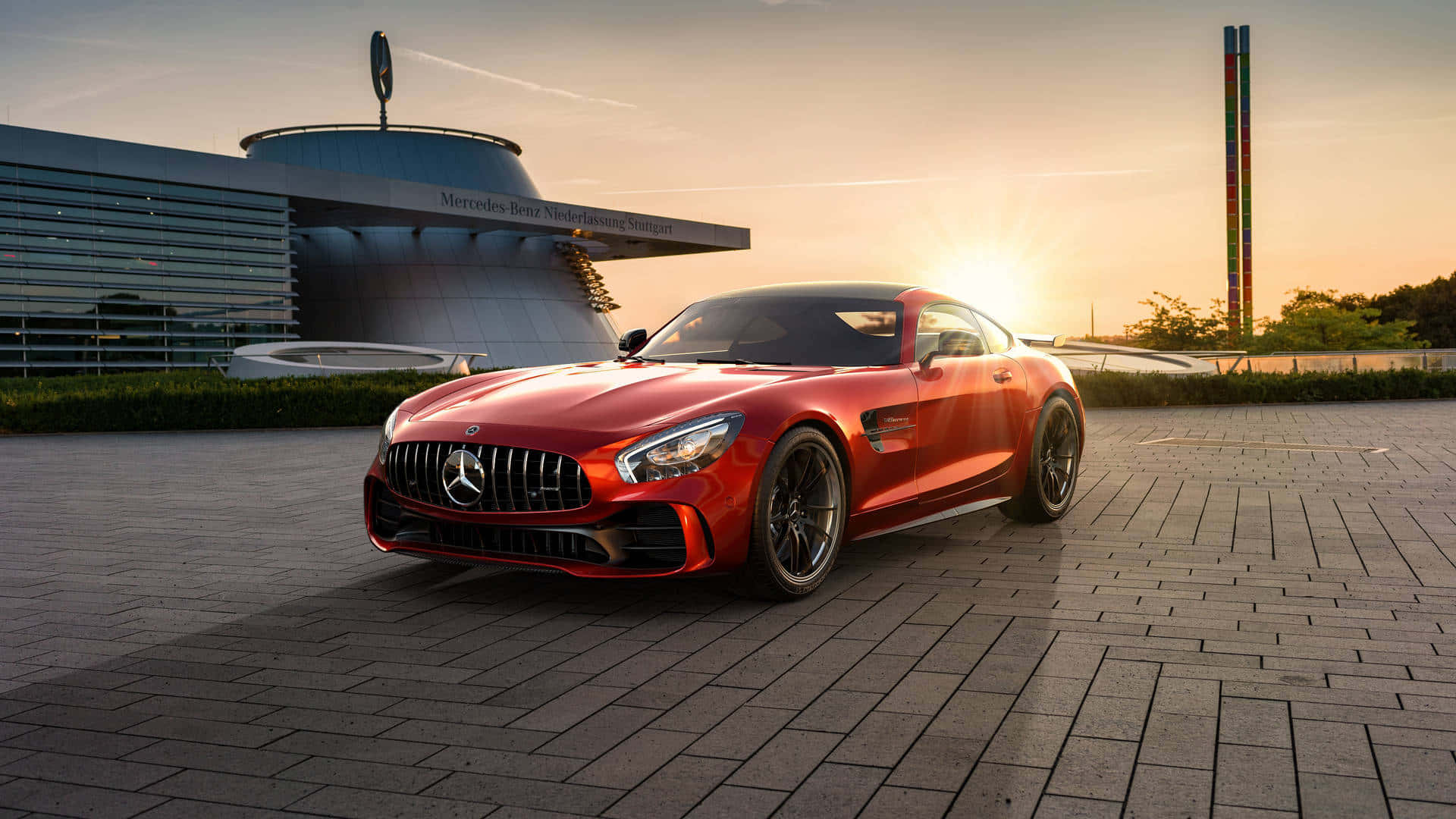 Gtr 桌布 壁紙 — 一輛鮮紅色的 Mercedes-AMG GT 跑車在日落時分於鋪砌的廣場上閃閃發光，背景是標誌性的梅賽德斯-奔馳博物館。