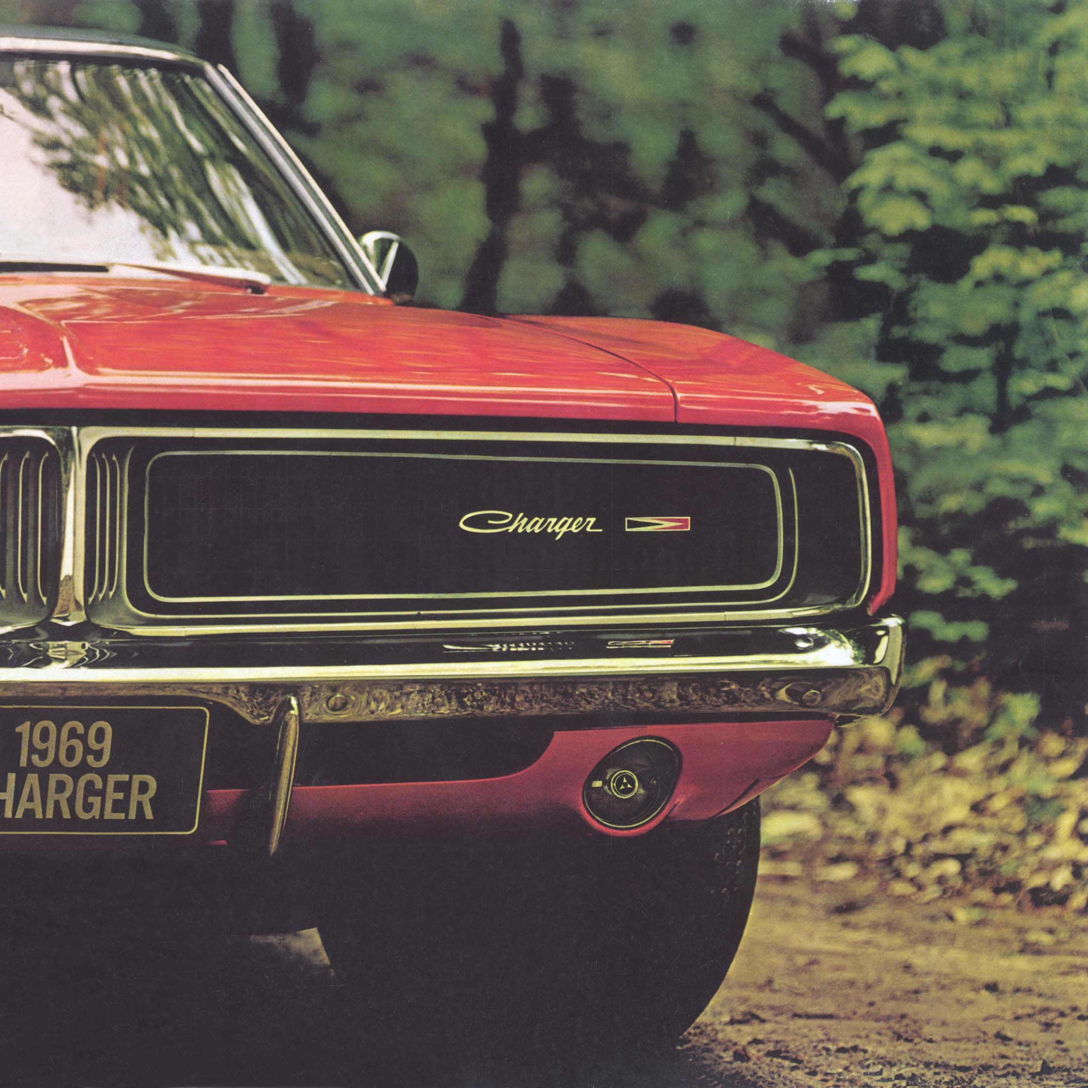 Dodge Charger 桌布 壁紙 — 一輛鮮紅色的1969年道奇Charger停泊在泥濘小徑上，周圍環繞著茂密的綠樹的特寫。