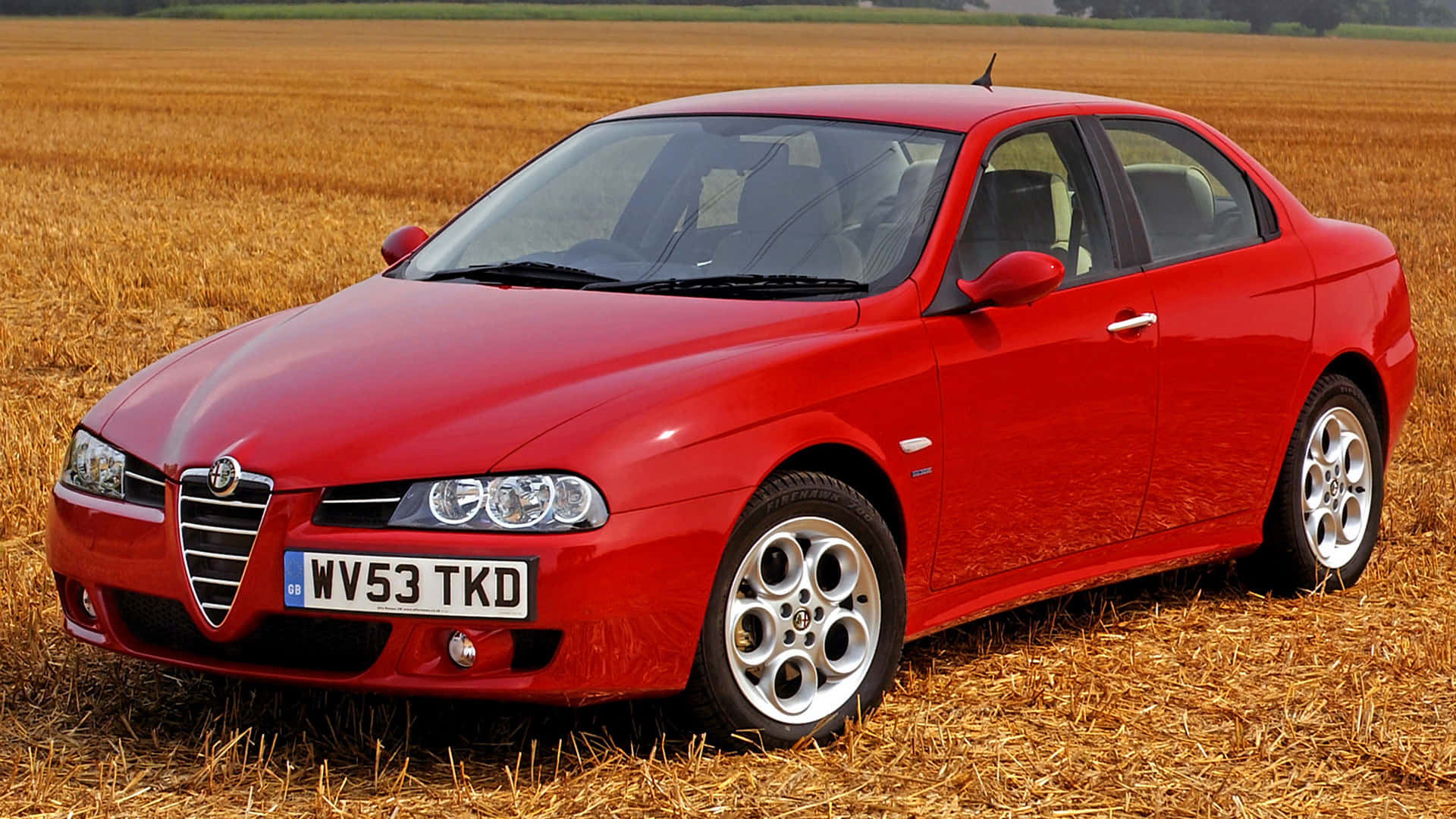 Alfa Romeo 156 桌布 壁紙 — 一輛鮮紅色的Alfa Romeo房車停泊在金色麥田裏，在明亮的日光下。