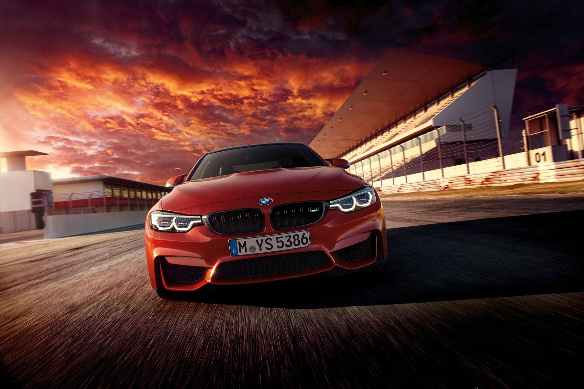 Sports Car 桌布 壁紙 — 一輛鮮紅色的BMW M4在火燒般的日落天空下，伴隨著戲劇性的雲彩，在賽道上飛馳。