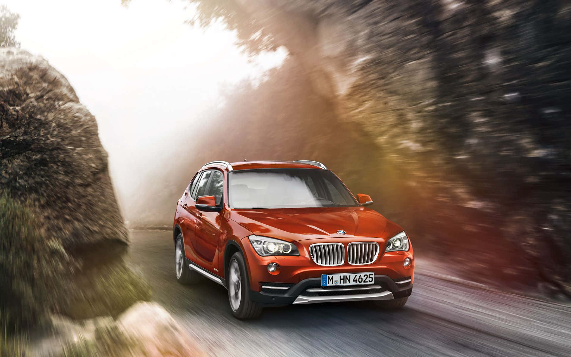 Bmw X1 桌布 壁紙 — 一輛鮮紅色的BMW X1 SUV在森林道路上疾馳，帶有動態模糊和陽光照耀的樹木。