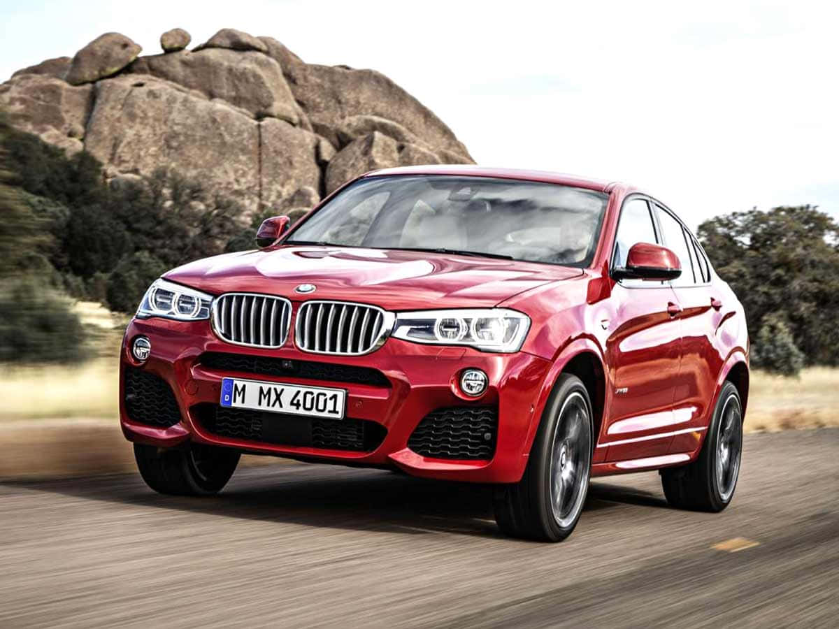 Bmw X4 桌布 壁紙 — 一輛鮮紅色的BMW X4 SUV在塵土飛揚的道路上疾馳，背景是巨大的岩石結構和稀疏的樹木。