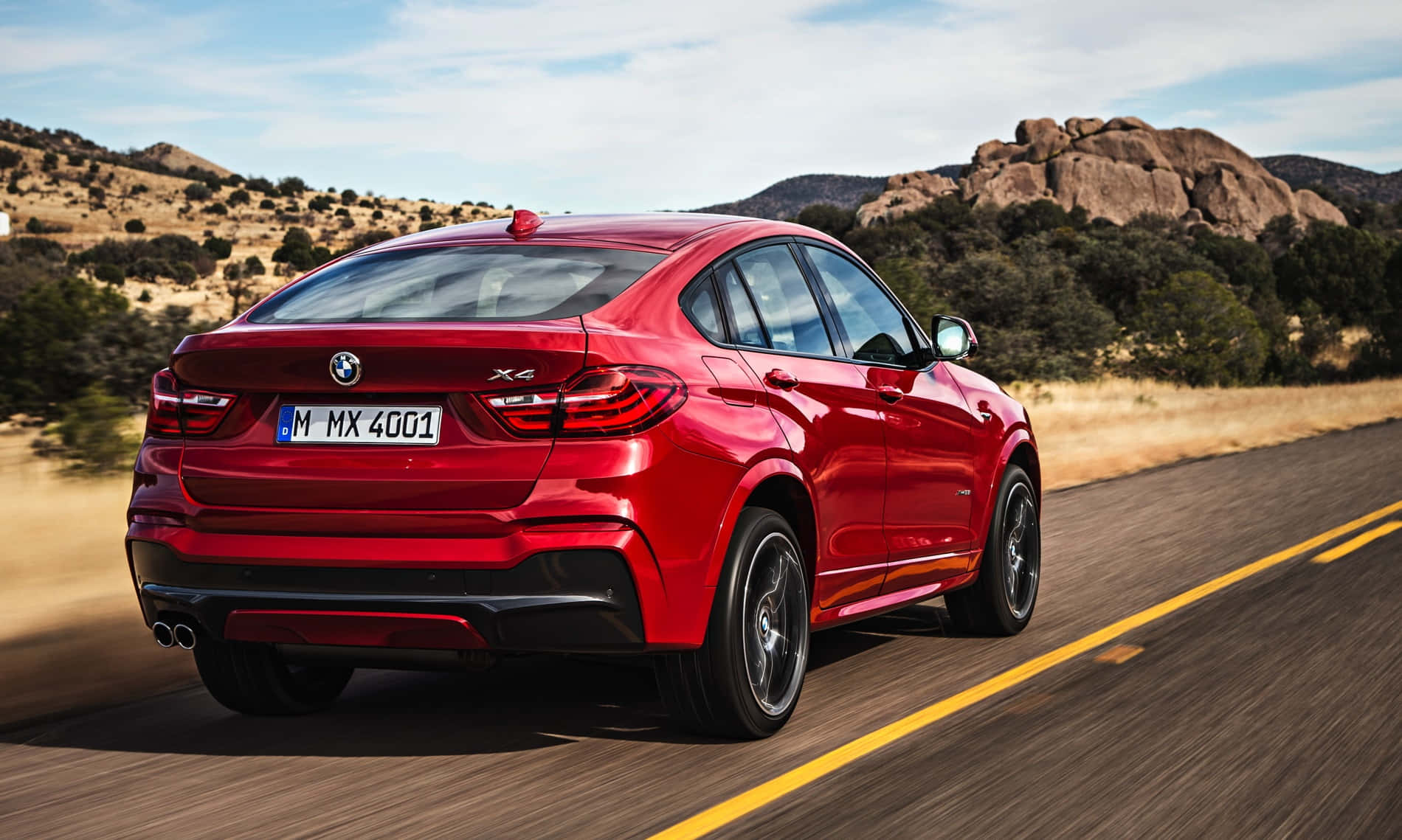 Bmw X4 桌布 壁紙 — 一輛鮮紅色的BMW X6 M在晴朗藍天下，沿著一條有岩石山丘和乾燥灌木的沙漠高速公路行駛。
