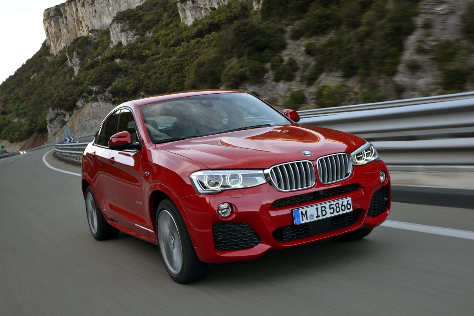 Bmw X4 桌布 壁紙 — 一輛鮮紅色的BMW X6沿著蜿蜒的山路行駛，兩旁是翠綠的懸崖和模糊的護欄。