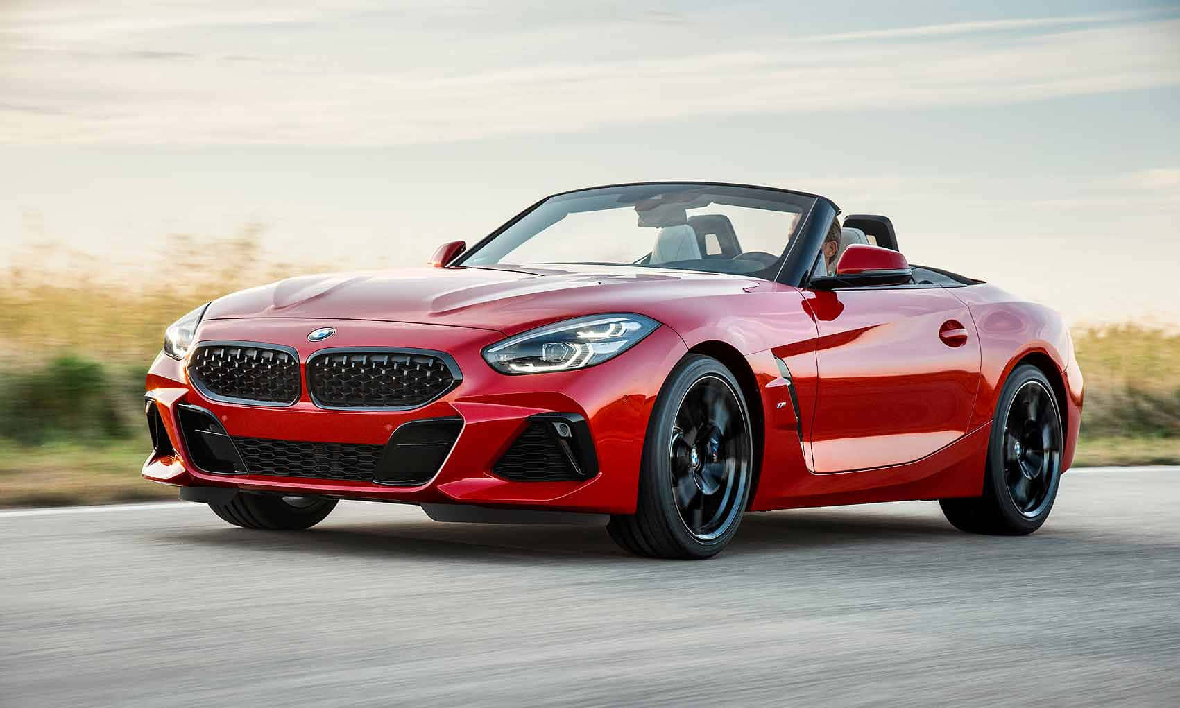 Bmw Z4 桌布 壁紙 — 一輛鮮紅色的BMW Z4開篷跑車在柔和天空下，沿著一條有模糊金色草叢的道路飛馳。