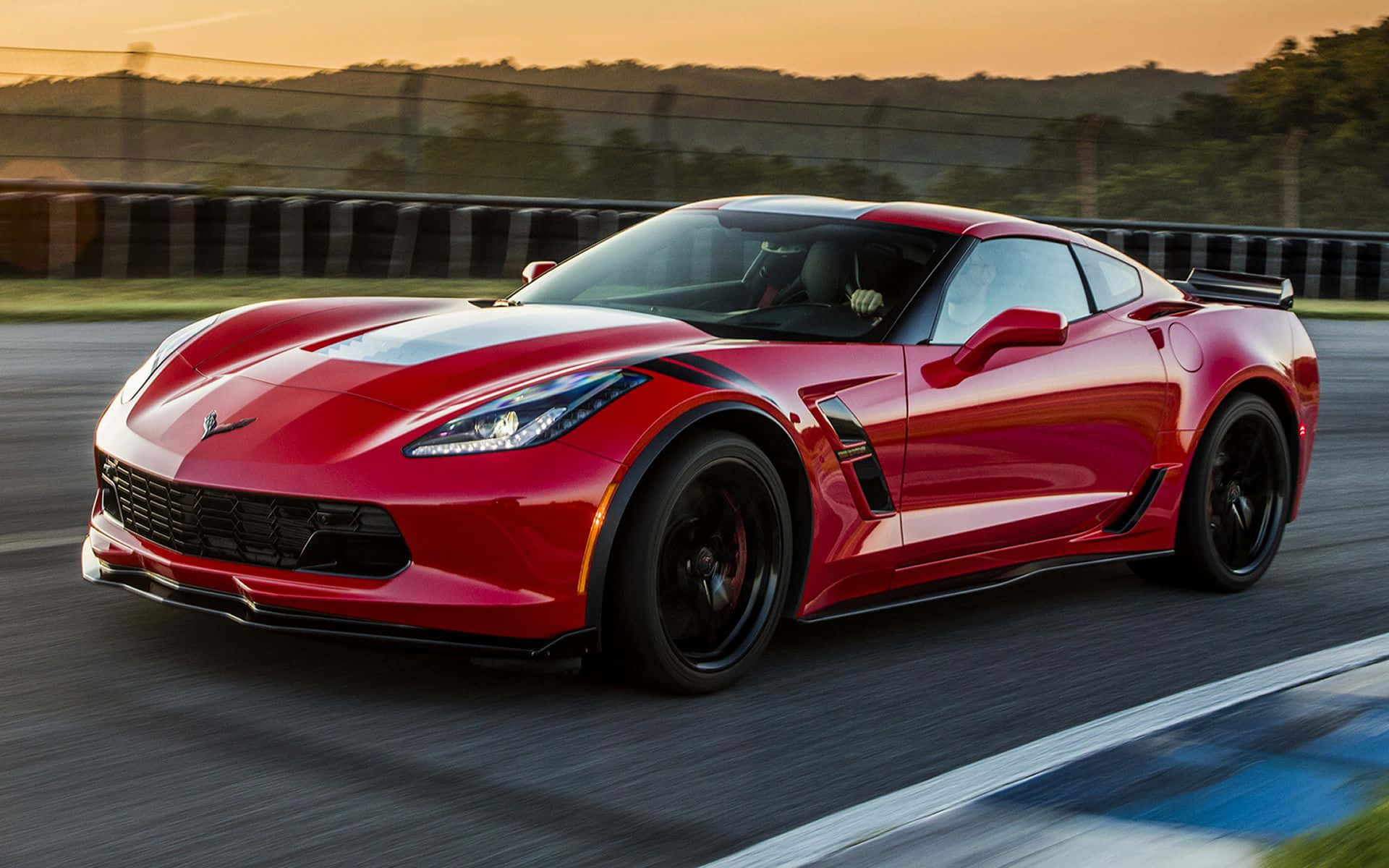 Chevrolet Corvette Grand Sport 桌布 壁紙 — 一輛鮮紅色的Corvette跑車在日落時分沿著賽道飛馳，動態模糊效果凸顯其力量與流線型設計。