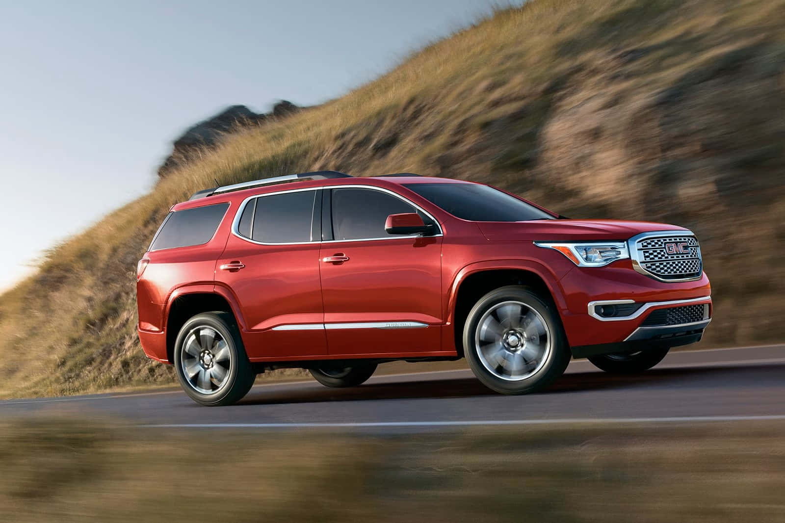 Gmc Acadia 桌布 壁紙 — 一輛鮮紅色的GMC Acadia SUV在蜿蜒的道路上疾馳，背景是模糊的金色山丘。