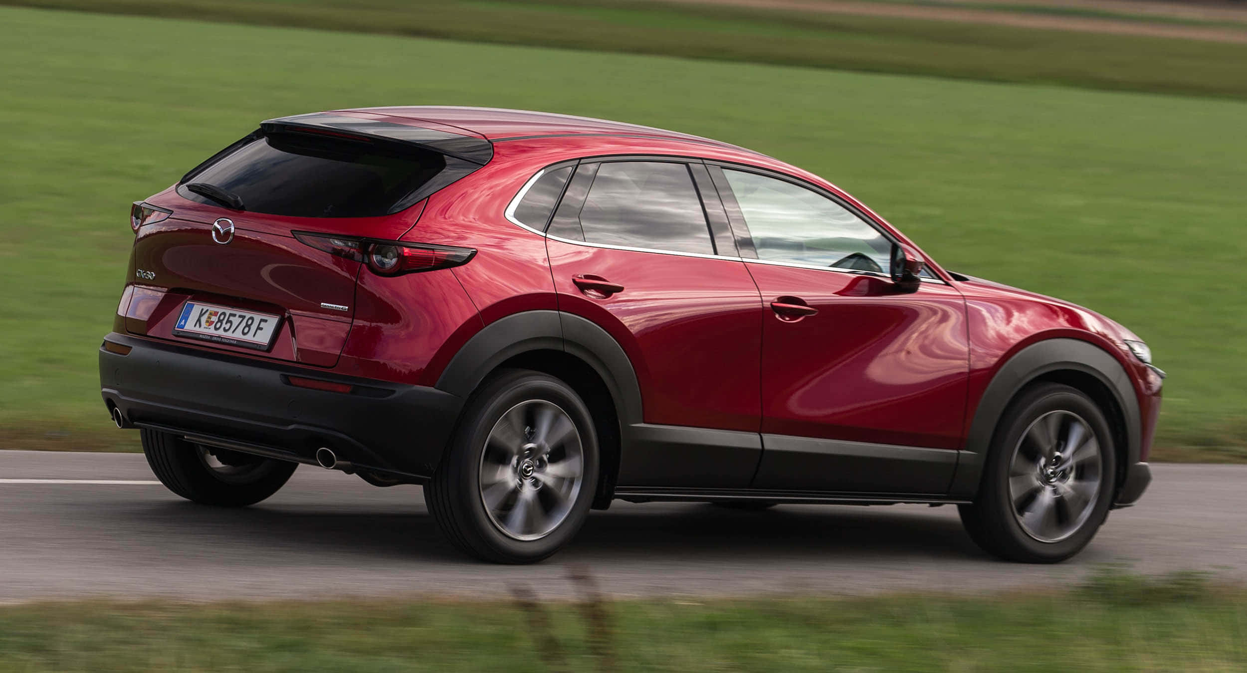 Mazda Cx-30 桌布 壁紙 — 一輛鮮紅色的Mazda CX-30 SUV在鄉村道路上行駛，背景是模糊的綠色田野。