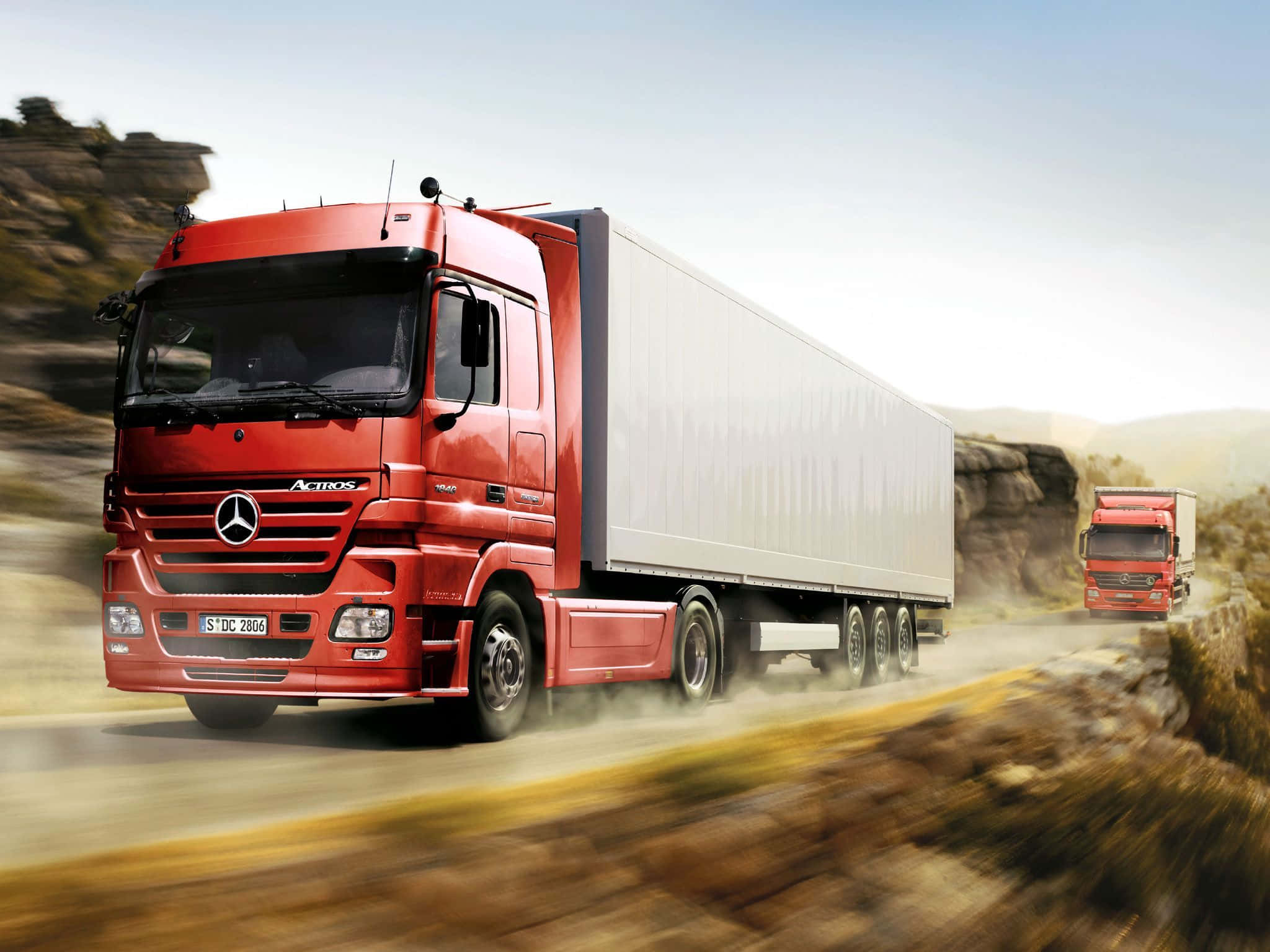 貨車 桌布 壁紙 — 一輛鮮紅色的Mercedes-Benz Actros貨車在塵土飛揚的山路上疾馳，後面緊跟著另一輛貨車。