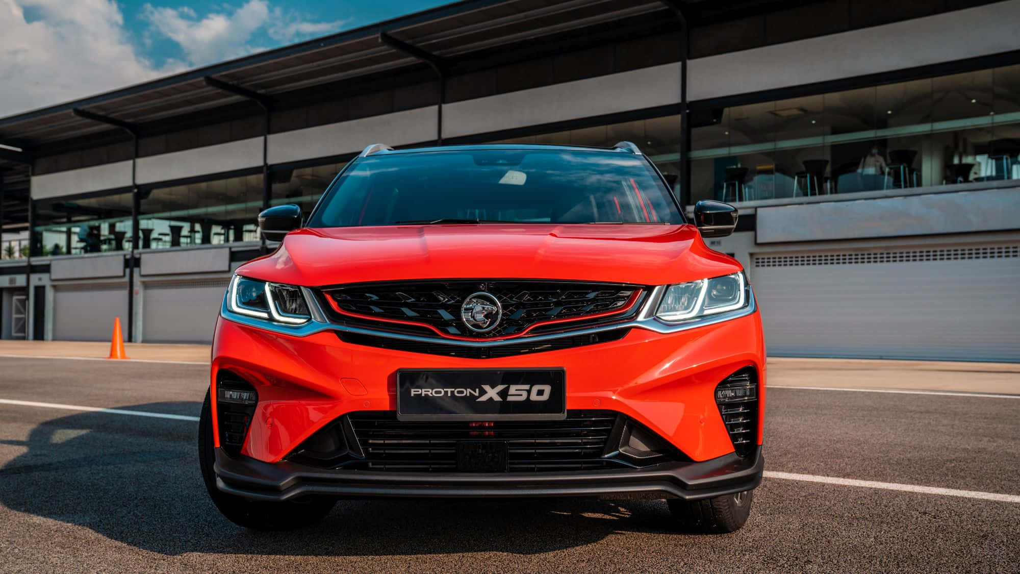 Proton 桌布 壁紙 — 一輛鮮紅色的Proton X50 SUV在晴朗藍天和零星白雲下的賽道上向前行駛。