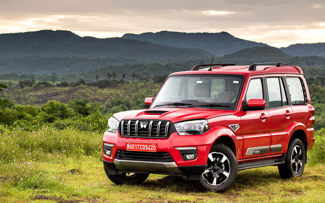 Mahindra Scorpio 桌布 壁紙 — 一輛鮮紅色的SUV停泊在草地上，背景是起伏的綠色山丘和多雲的天空。