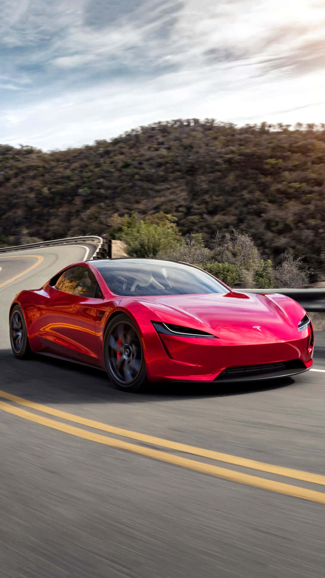tesla 桌布 壁紙 — 一輛鮮紅色的Tesla Roadster在部分多雲的天空下沿著蜿蜒的山路飛馳。